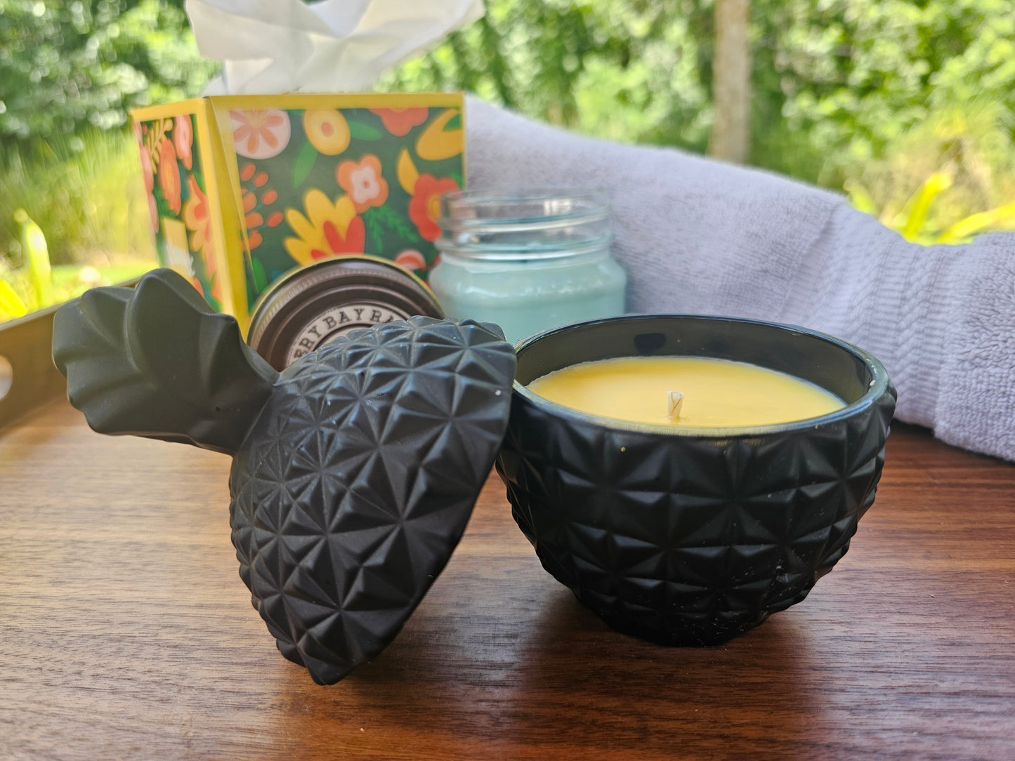 Black textured candle holder with a lit candle on a wooden surface, with a blurred background.