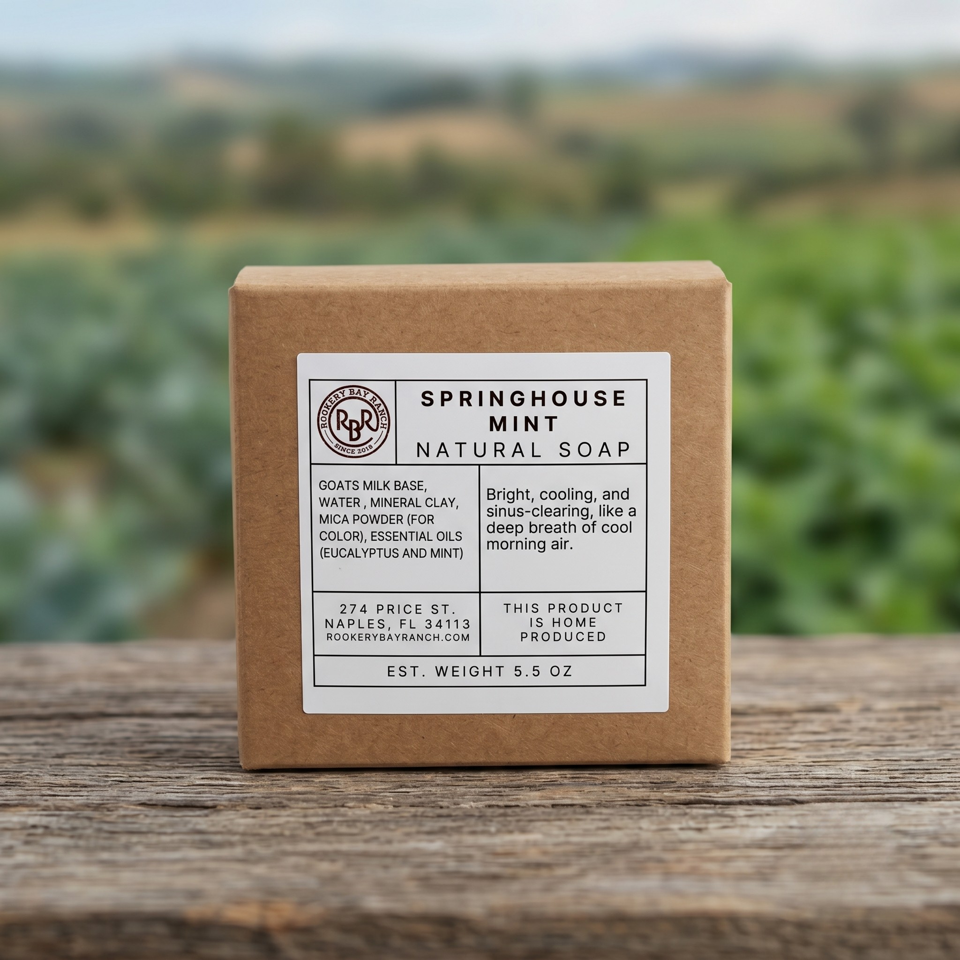 Box of Springhouse Mint natural soap on a wooden surface with a blurred green field background